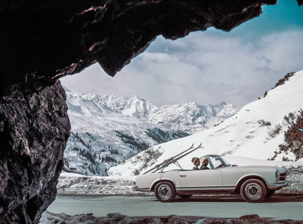 Mercedes-Benz SL Pagode (W 113). Photo de genre dans un décor alpin enneigé avec des équipements de sports d'hiver à l'arrière de la voiture